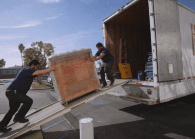 Professional movers are safely loading a large item into a moving truck using a ramp